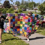 Person walking with colourful patchwork quilt in Napanee Pride march.
