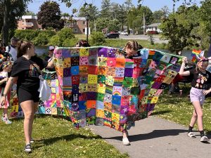 Person walking with colourful patchwork quilt in Napanee Pride march.